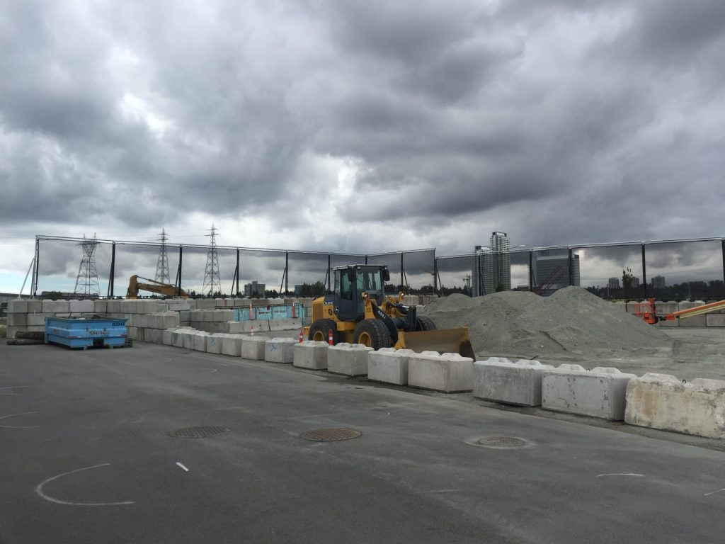 A construction site with heavy machinery and concrete barriers under a cloudy sky