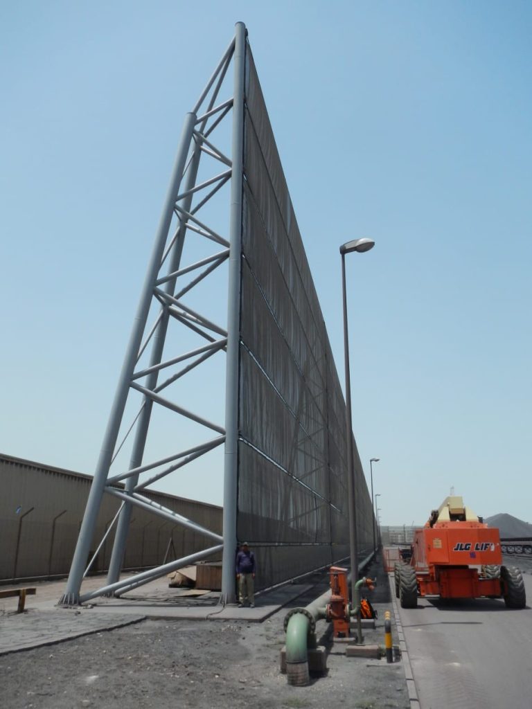 A tall, triangular metal structure stands next to a road with an orange JLG lift nearby