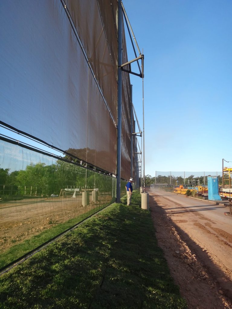 A large wind fence stretches along a dirt road with a person standing nearby