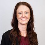 A woman with long brown hair and a burgundy top against a plain background