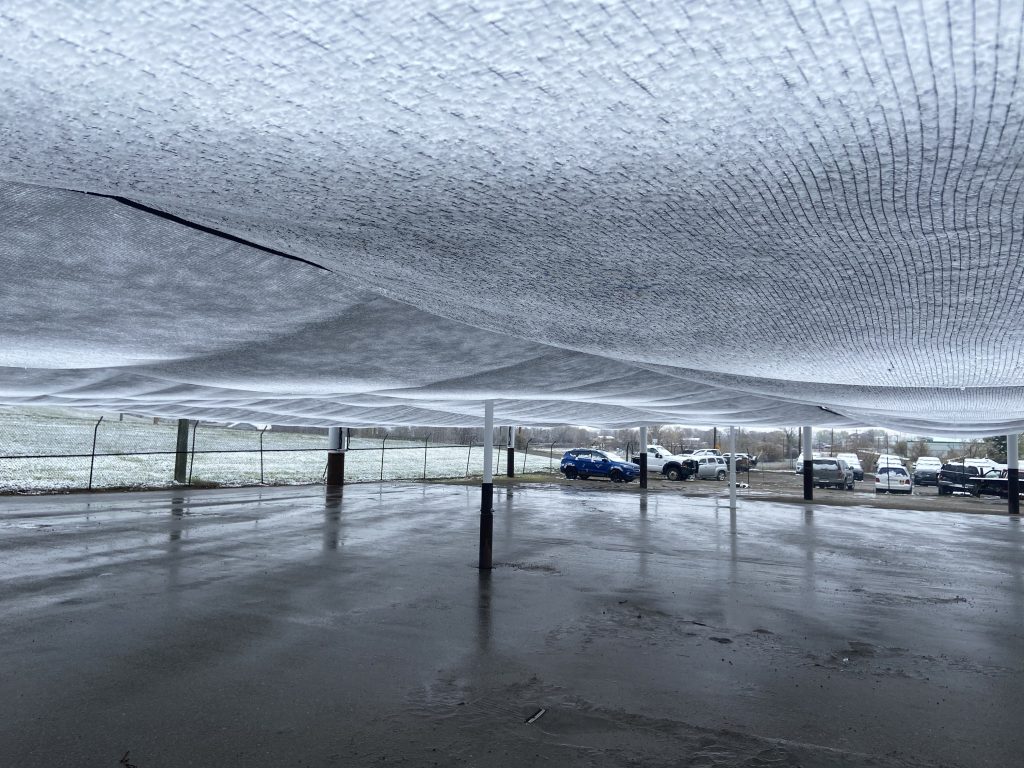 A large canopy structure with vehicles parked underneath on a wet surface