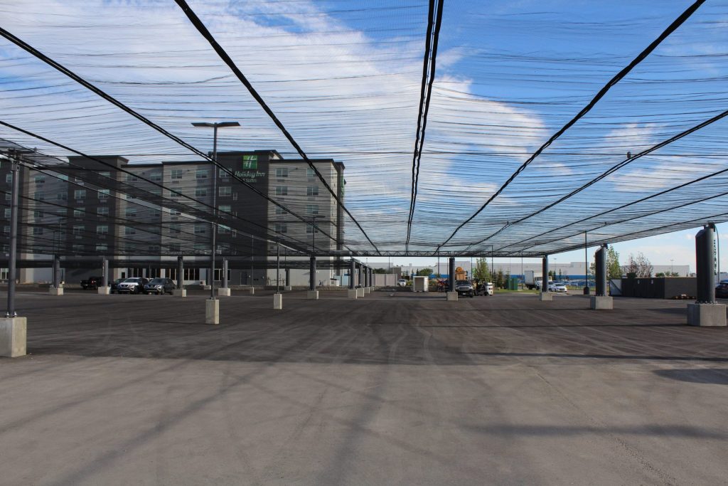 A parking lot with a large overhead netting structure supported by concrete pillars