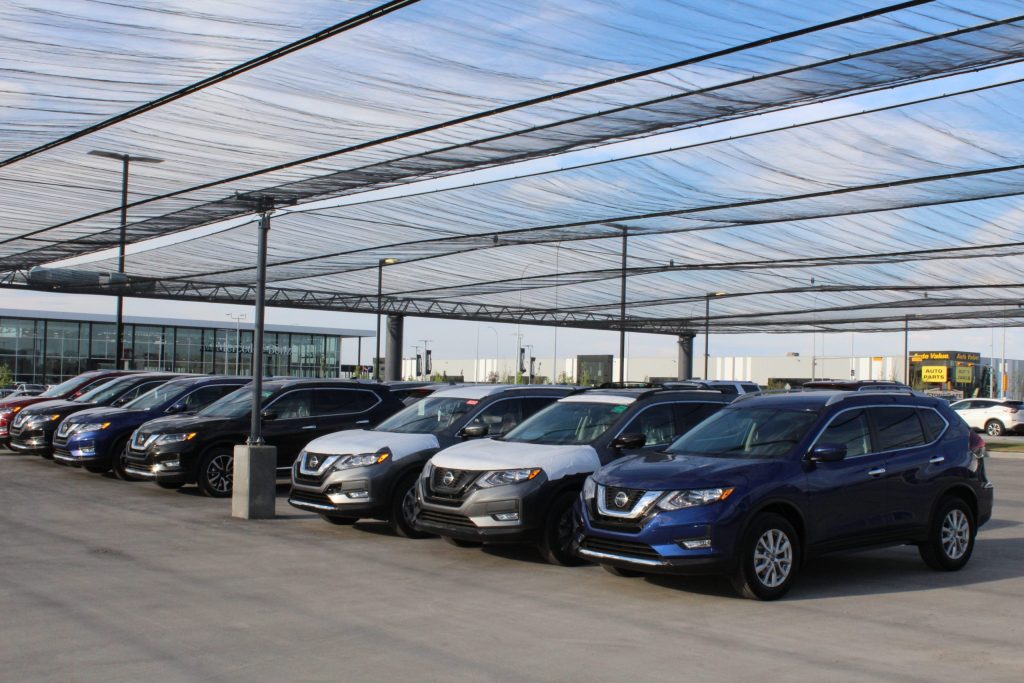 Several cars parked under a large, translucent canopy at a dealership