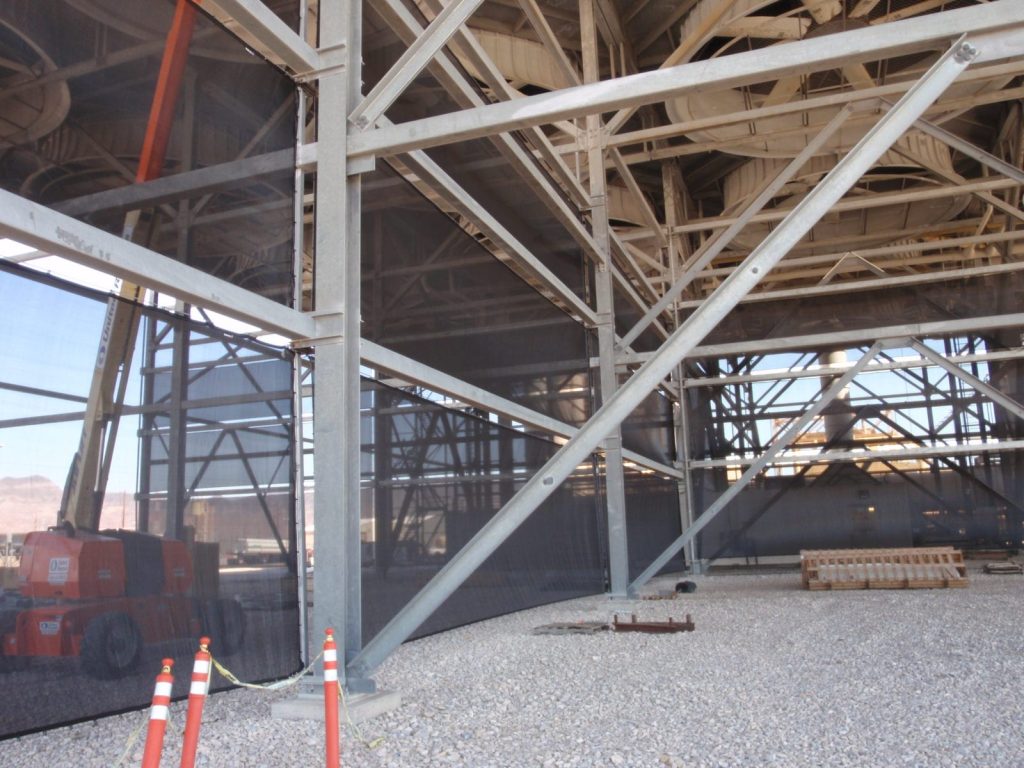 Metal framework and netting structure with construction equipment and safety cones visible