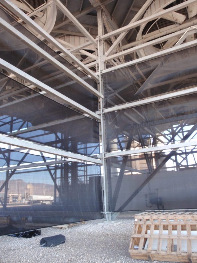 Industrial structure with metal framework and dark mesh panels, gravel ground, and wooden pallet