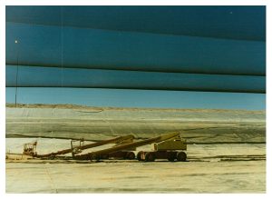 A large, light-colored tarp covers the ground with two construction vehicles on top
