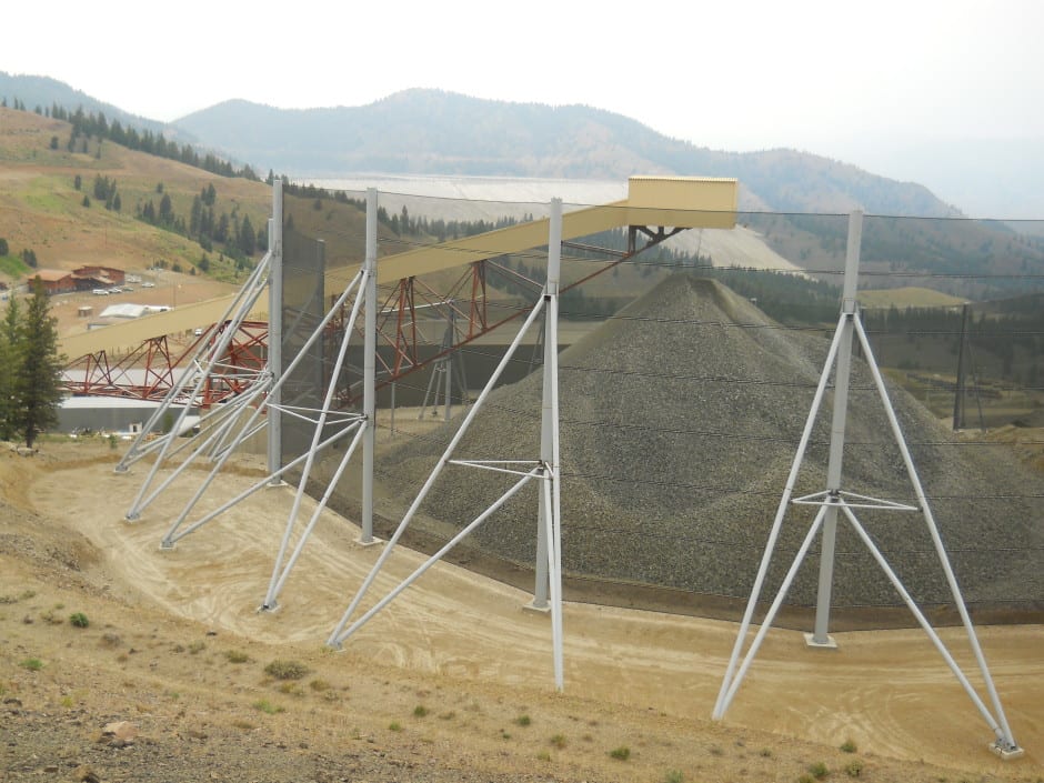 A large gravel pile is covered by a wind fence supported by metal poles
