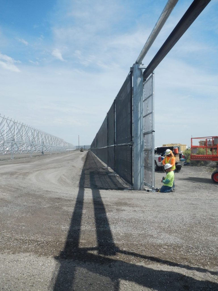 Two workers installing a gate in a long fence line on a sunny day
