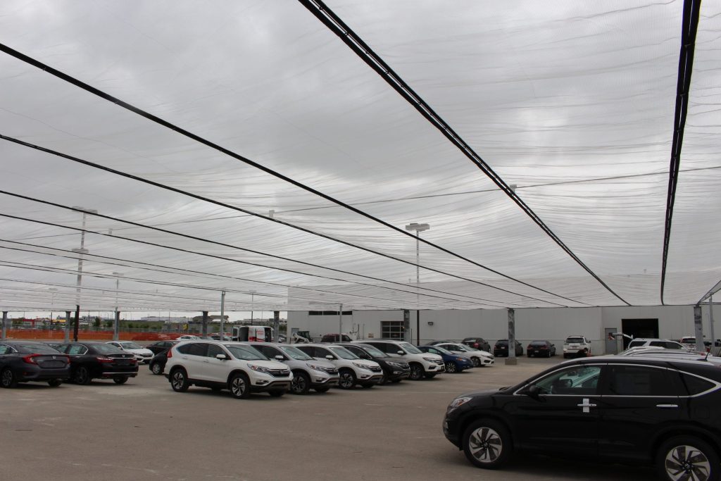 Cars parked under a large translucent canopy on a cloudy day