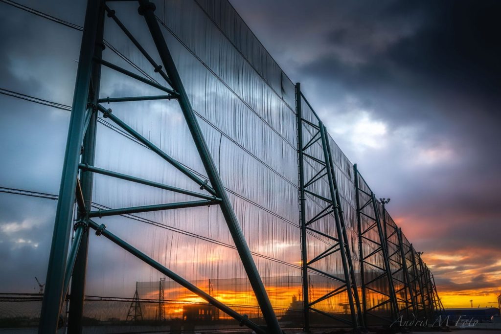 A large industrial fence structure against a dramatic sunset sky