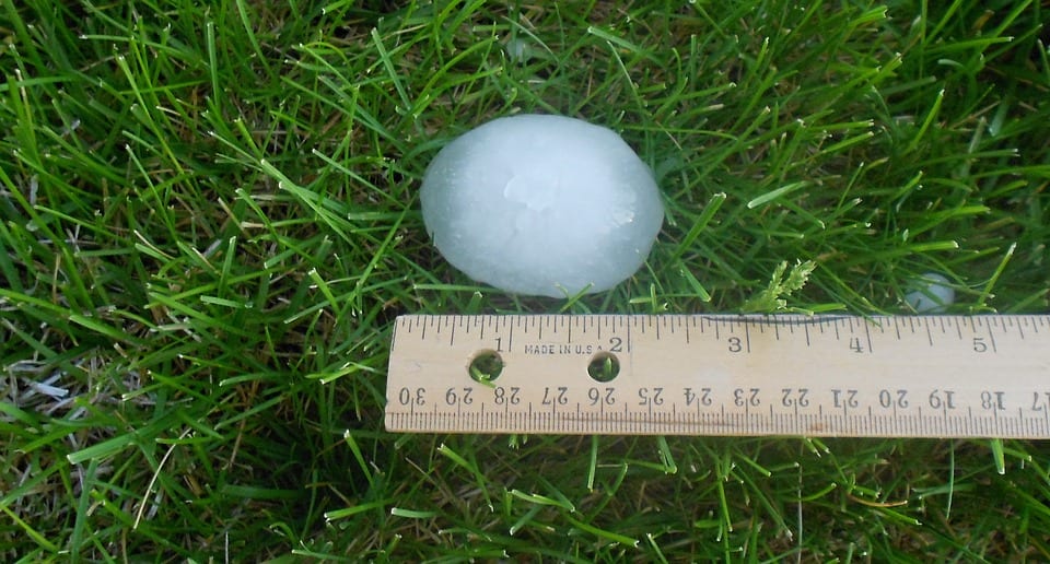 Large hailstone next to a ruler on grass, measuring around 2 inches in diameter.