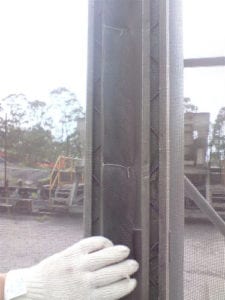 A gloved hand holds a mesh screen next to a metal structure outdoors.