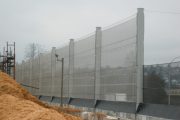 A tall, translucent wind fence stretches along a construction site with a pile of wood chips in the foreground