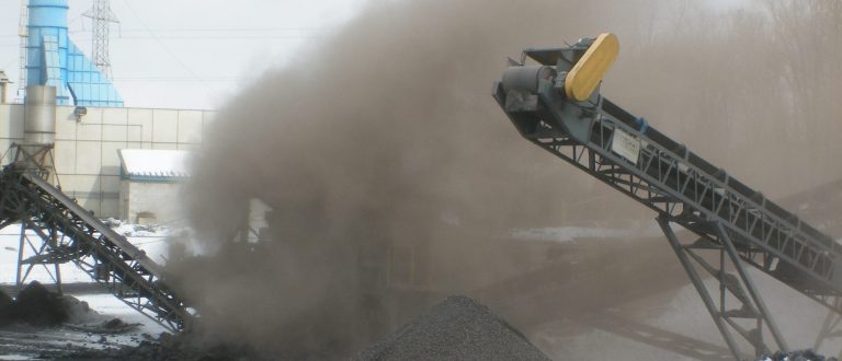 Dust cloud from conveyor belt at industrial site with snow on ground