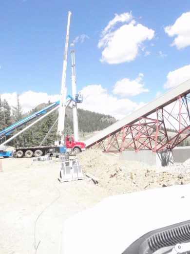 A crane and conveyor belt structure at a construction site with a mountainous backdrop