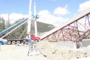 A crane and conveyor belt structure at a construction site with a mountainous backdrop