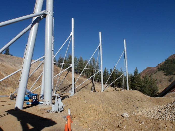 Large metal poles and beams are installed on a dirt slope with trees in the background