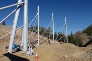 Large metal poles and beams are installed on a dirt slope with trees in the background