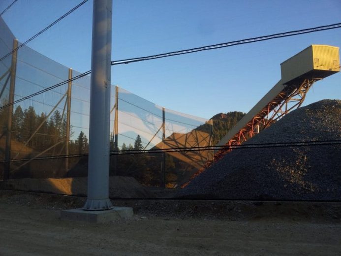 A gravel pile, conveyor belt, and wind fence under a clear sky