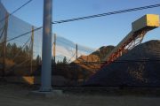 A gravel pile, conveyor belt, and wind fence under a clear sky