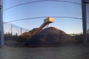 A large pile of gravel is covered by a netted structure supported by metal poles