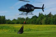 A helicopter hovers above a field, carrying a large black net suspended by ropes