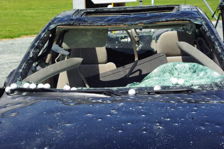 A car with a severely damaged windshield and hood, covered in golf balls