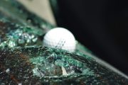 A golf ball rests on shattered glass, likely from a hail impact test