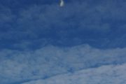 A helicopter releases a substance into the air above trees and clouds