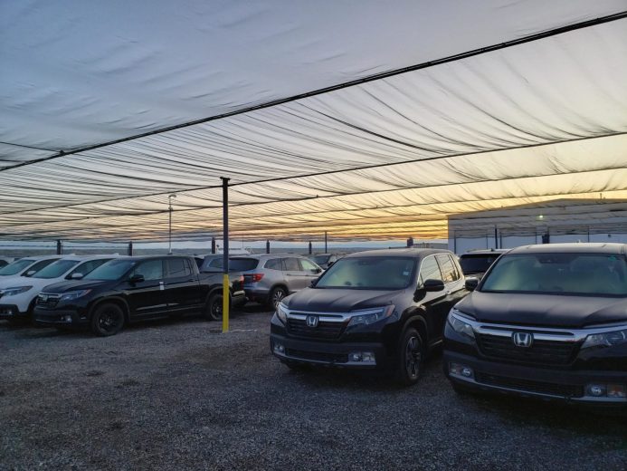 Cars parked under a large, translucent canopy at sunset