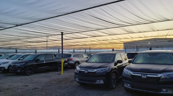 Cars parked under a large, translucent canopy at sunset