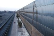 A long industrial wind fence stretches alongside a road with a red car driving past