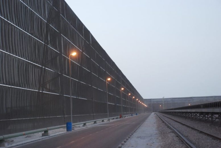 A long industrial wind fence stretches alongside a road and railway tracks