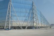 A large blue industrial wind fence supported by white metal framework stands on a dusty ground