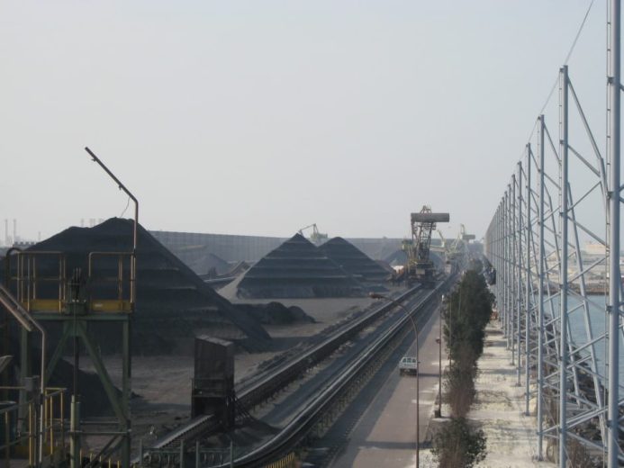 Coal piles and conveyor belts at an industrial site with a large wind fence
