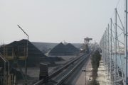 Coal piles and conveyor belts at an industrial site with a large wind fence