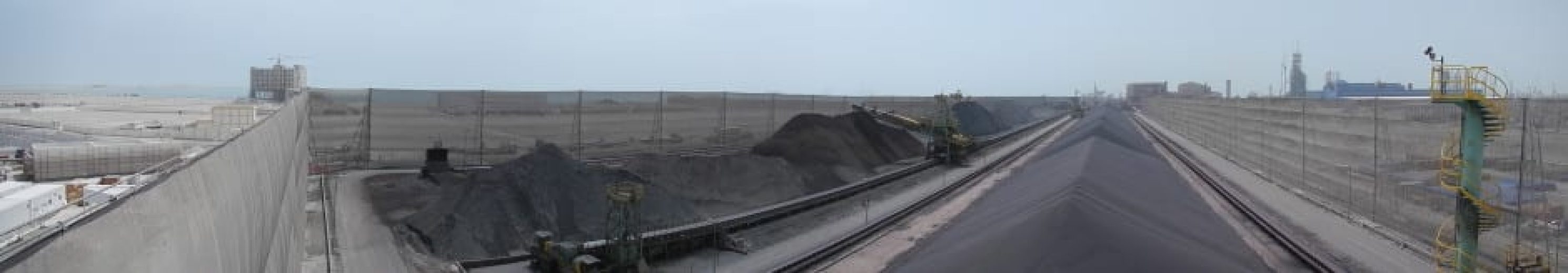A panoramic view of an industrial site with large piles of coal and wind fences