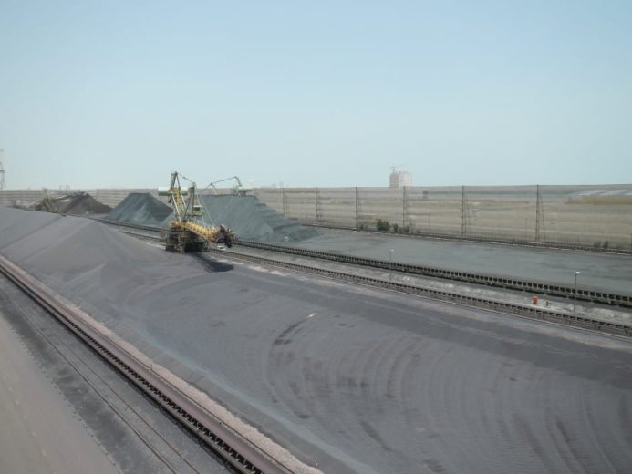 Aerial view of coal piles and machinery at an industrial site with wind fences
