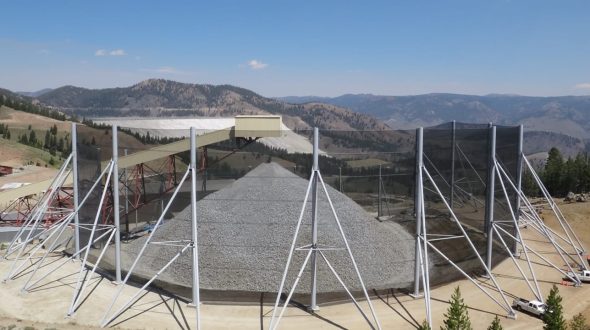 A large industrial structure with metal supports and netting stands against a mountainous backdrop