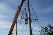 A crane lifts workers in a basket to the top of a tall metal pole