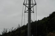 A tall metal pole with guy wires and a ladder, surrounded by construction equipment and workers
