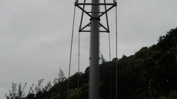 A tall metal pole with guy wires and a ladder, surrounded by construction equipment and workers