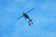 A helicopter flies against a blue sky with a bucket suspended below it