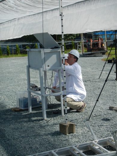 A person in a white shirt and hard hat works on equipment under a canopy