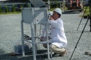 A person in a white shirt and hard hat works on equipment under a canopy
