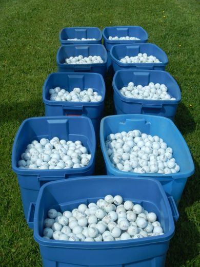 Nine blue bins filled with white golf balls on a grassy field