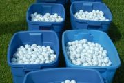 Nine blue bins filled with white golf balls on a grassy field