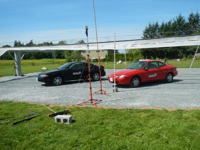 Two cars parked under a large white canopy structure in a grassy area
