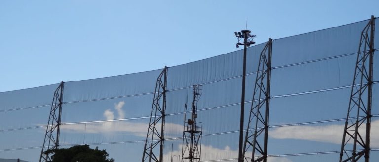 A large industrial wind fence stretches across the image against a clear blue sky