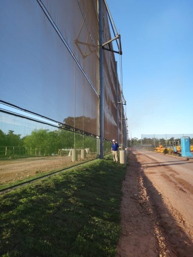 A large mesh fence runs alongside a dirt road with a person standing nearby